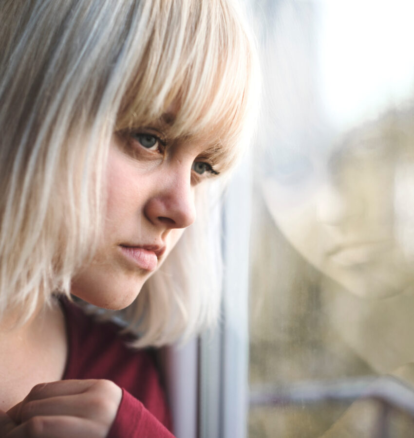 Close up of depressed young blond woman near window at home.  Sa